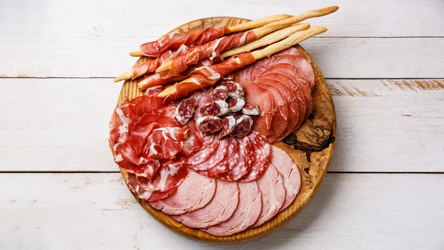 Above shot of different cuts of deli meats and salamis on a circular wooden board