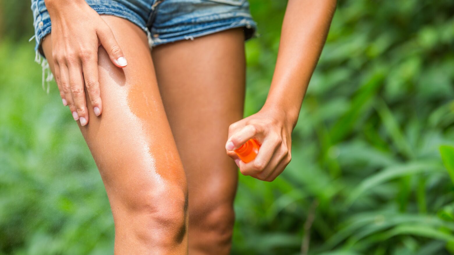 Woman applies a DEET-free spray to repel mosquitoes on her legs