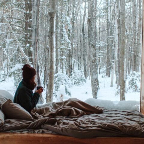 Woman looking out a large bedroom window to a winter landscape