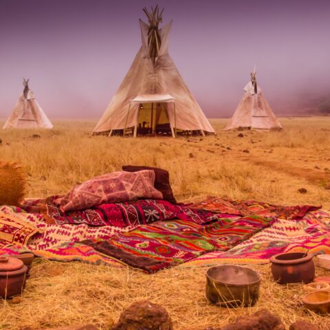 Blankets and cookware on the ground in front of 3 Native American teepees