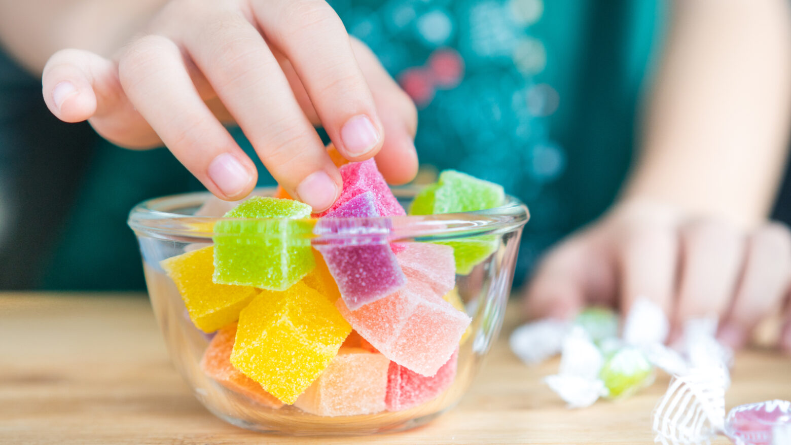 Close-up of a child's hand reaching into a bowl of colorful, sugary candies.