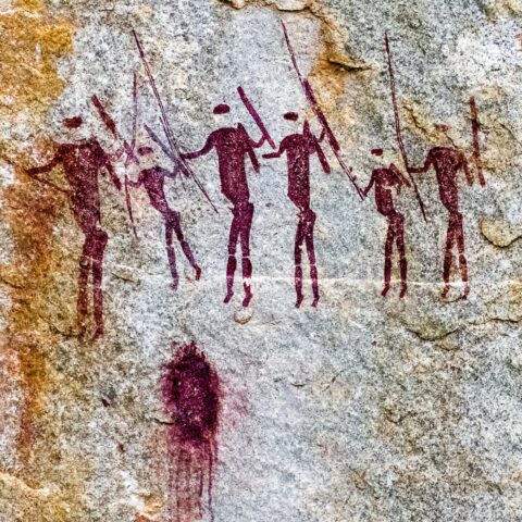 A rock painting of hunters with spears in red paint.
