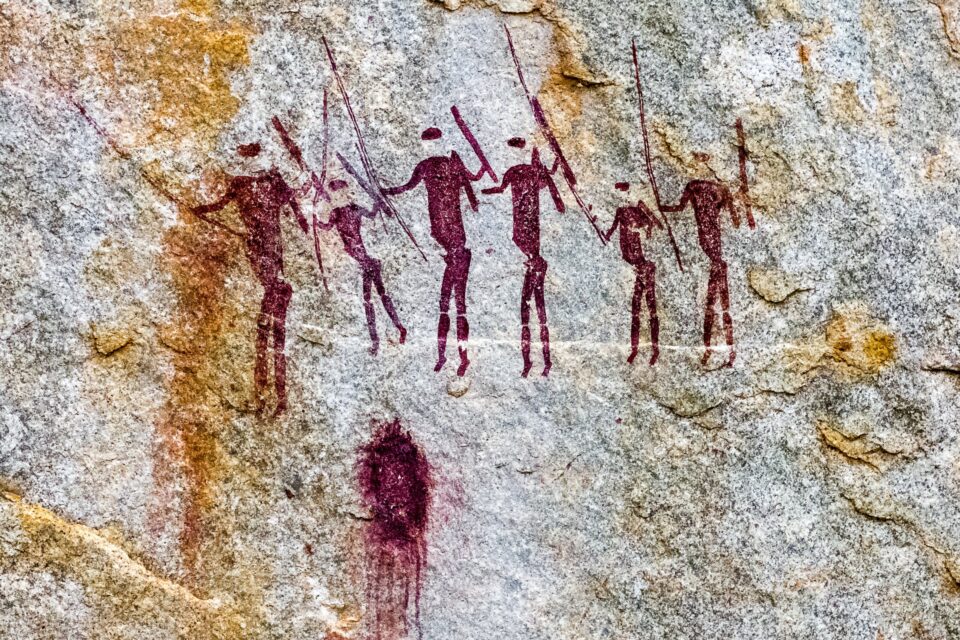 A rock painting of hunters with spears in red paint.