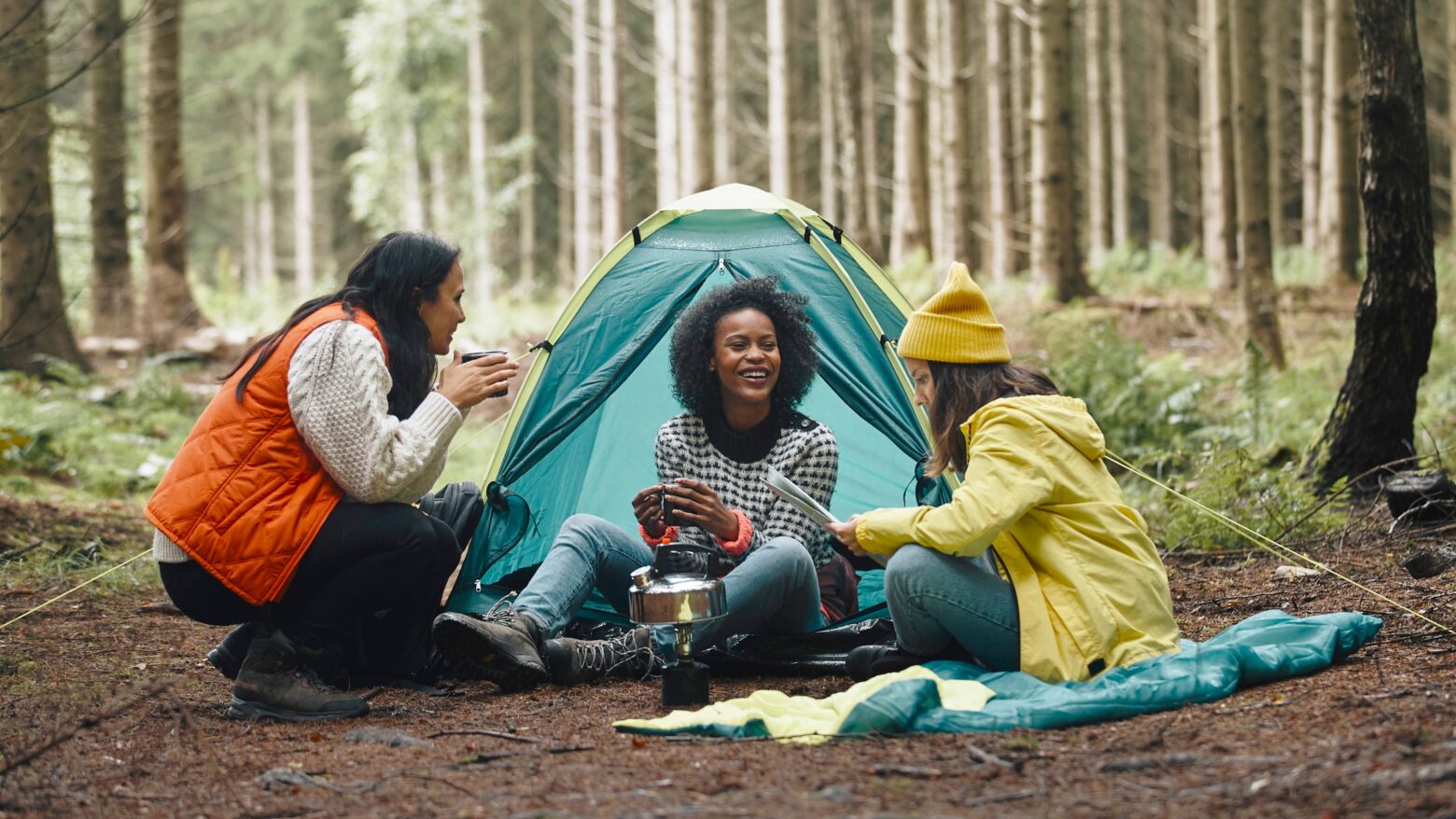Three women gather around a tent while camping