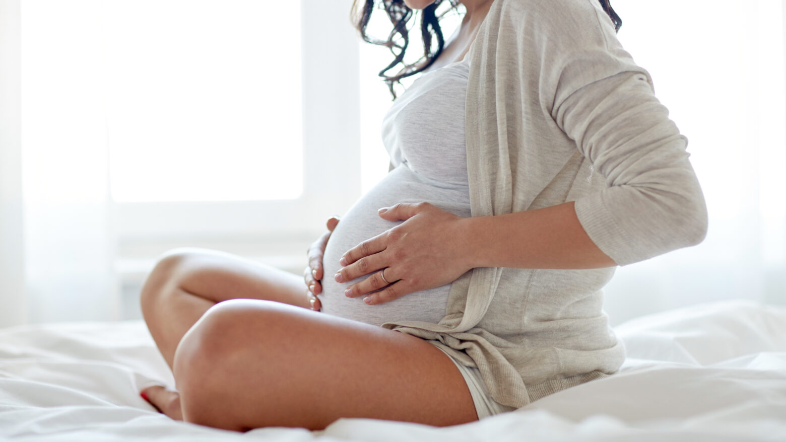 Pregnant woman sitting in bed with her hands on her abdomen