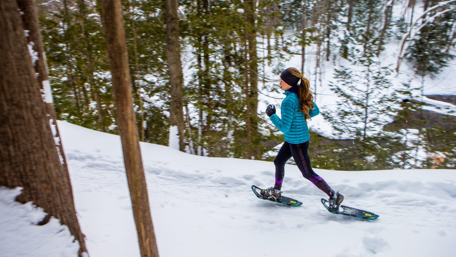 Woman snowshoe running through a snowy forest