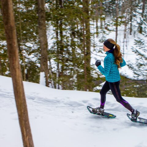Woman snowshoe running through a snowy forest