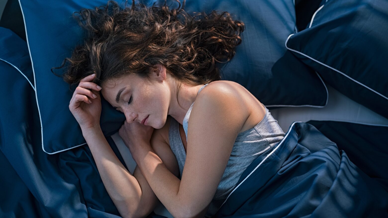 Woman asleep in a bed with dark blue sheets.