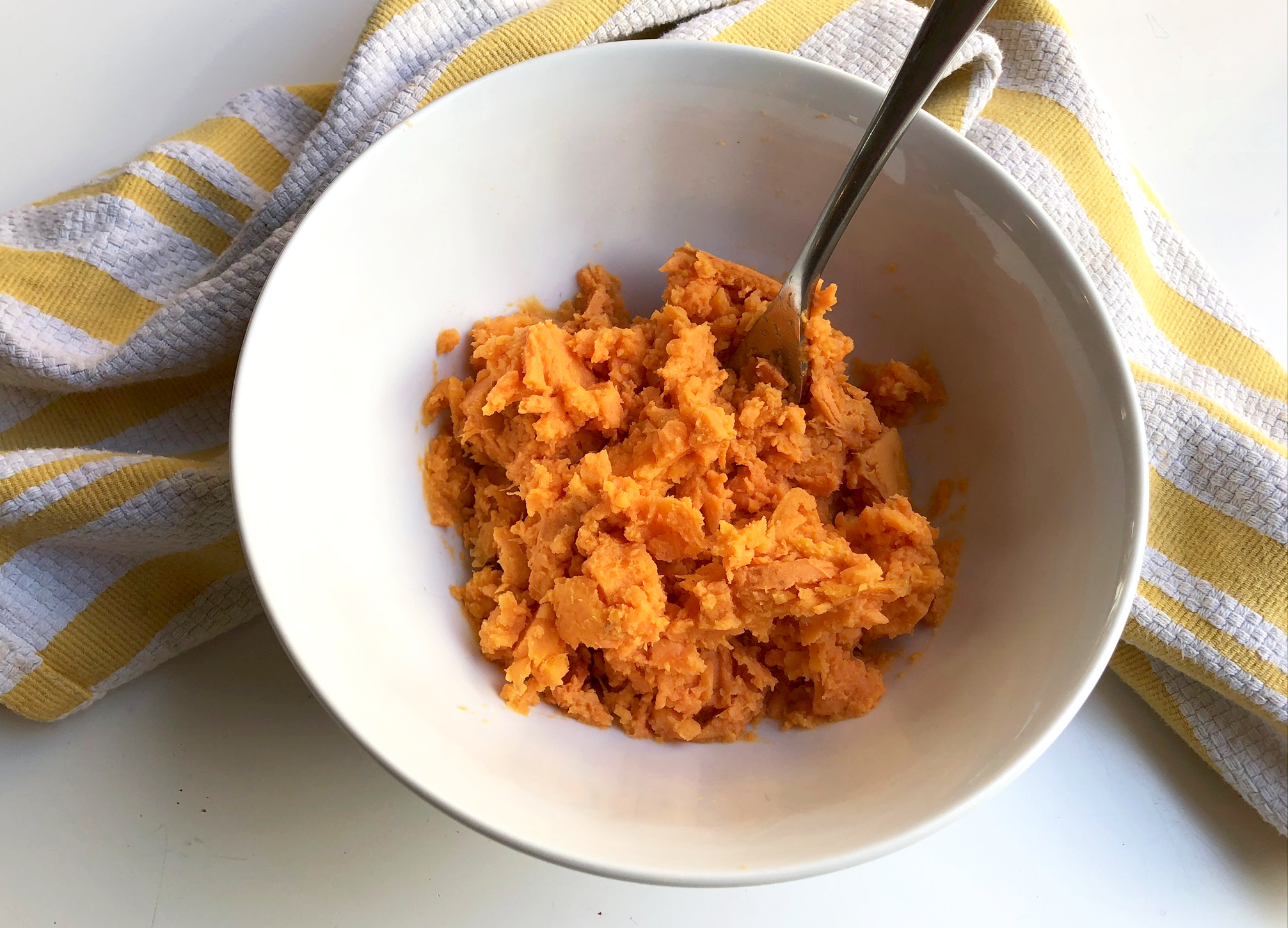 Sweet potato in a bowl being mashed up. 