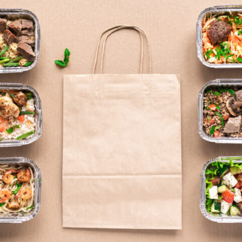 Above shot of different Paleo takeout meals in trays with a paper bag.