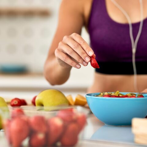 A woman in work-out attire makes herself a bowl of fruit.