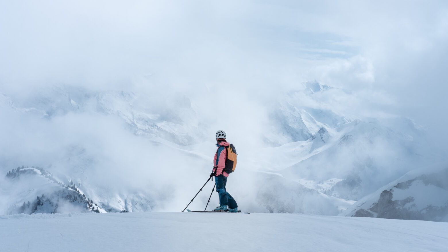 A skier looks out at white, cloud-covered mountains