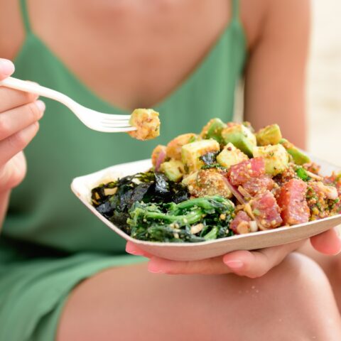 Close up of a woman eating a poke bowl at the beach.