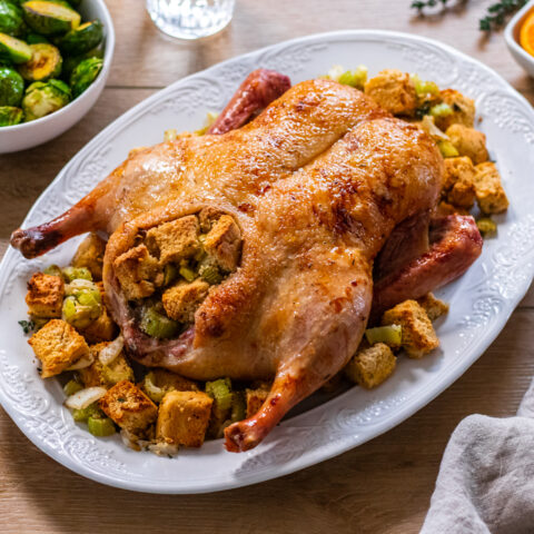 Orange Glazed Duck with Herb Stuffing, unsliced cooked duck on a plate.