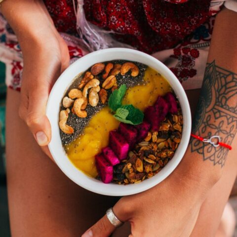Woman holding a colorful smoothie bowl topped with nuts.