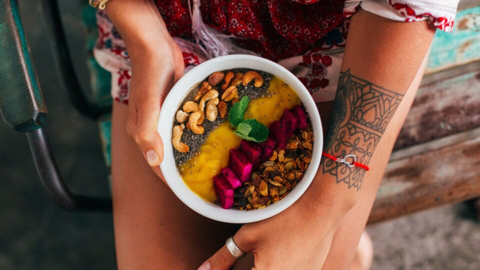 Woman holding a colorful smoothie bowl topped with nuts.