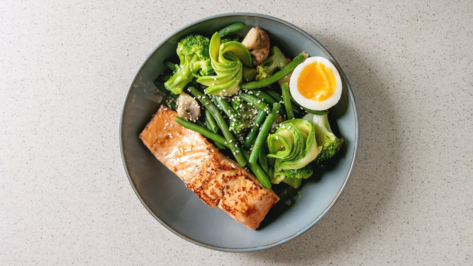 A keto-friendly bowl of salmon, a hard-boiled egg, green beans, avocado, and broccoli