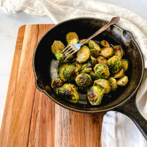 Roasted Brussels Sprouts recipe in a cast iron skillet on a wooden cutting board
