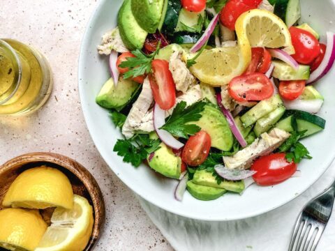 Cucumber & chicken salad from above, garnished with a twisted slice of lemon and parsley, next to a small wooden bowl of lemon wedges.