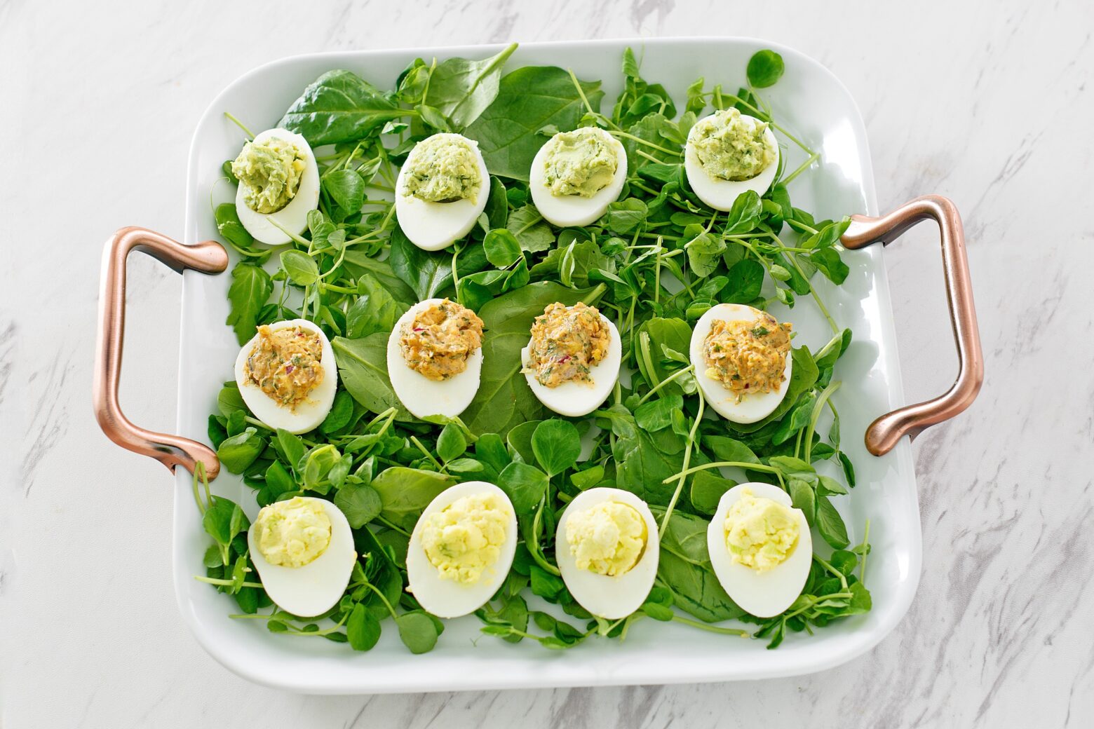 Three versions of deviled eggs arranged on a bed of greens.