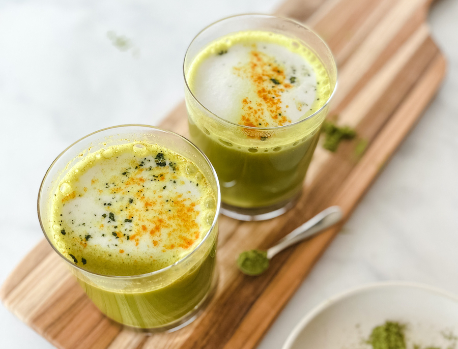 Two glasses of Golden Matcha Latte and a small silver spoon on a wooden serving board.