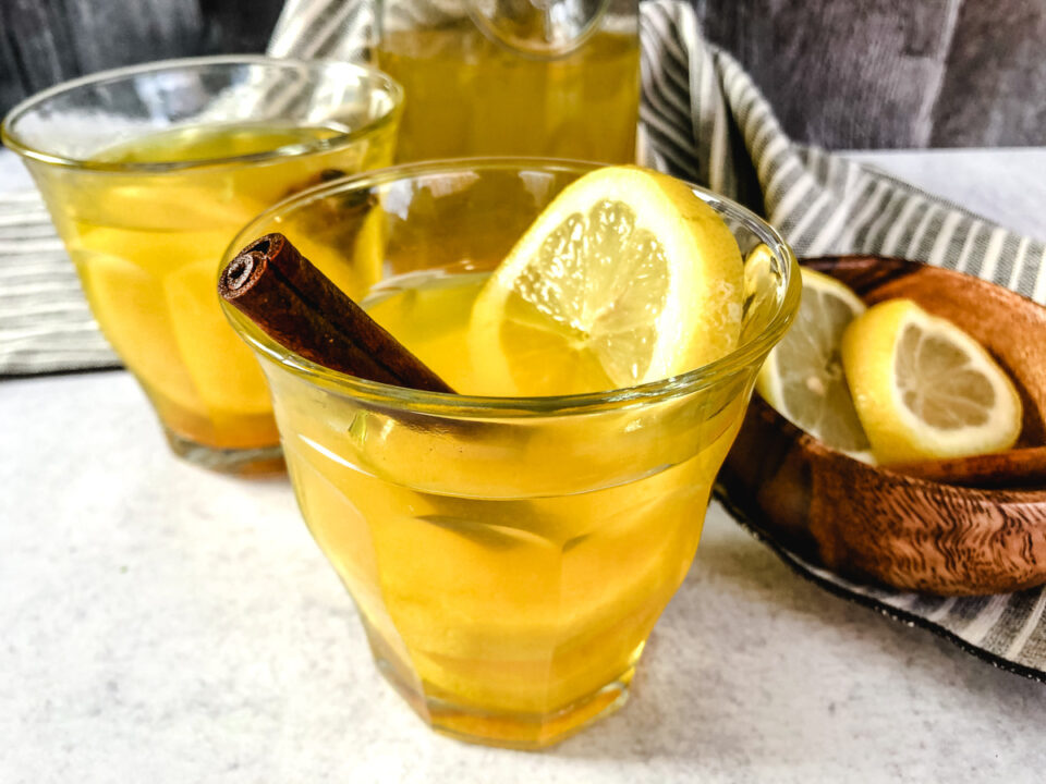 Two glasses of ginger turmeric tea with a slice of lemon and a cinnamon stick in one.