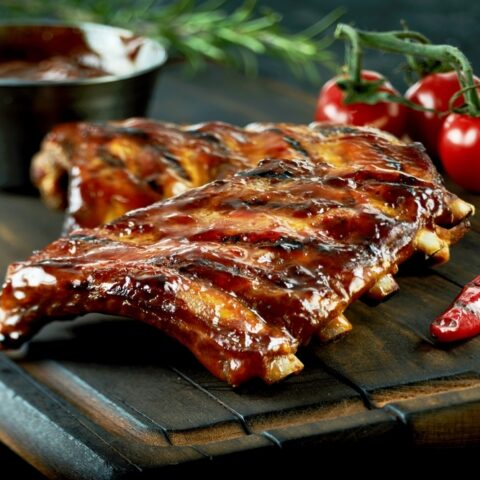 St. Louis style pork ribs on a wooden table next to vine tomatoes and a chili pepper.