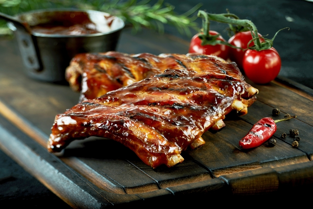 St. Louis style pork ribs on a wooden table next to vine tomatoes and a chili pepper.