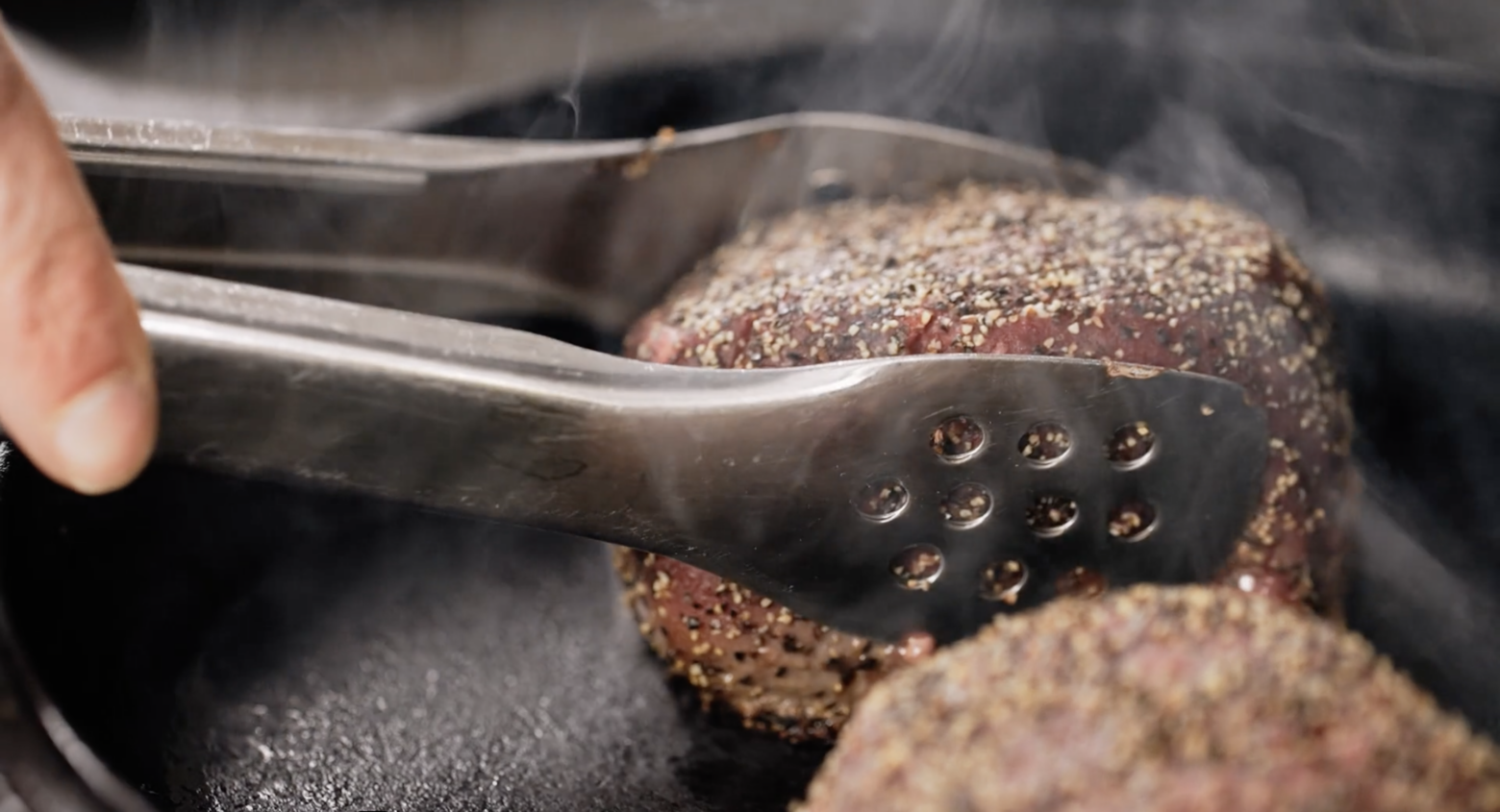 A peppercorn-crusted filet mignon sears in a cast iron skillet.
