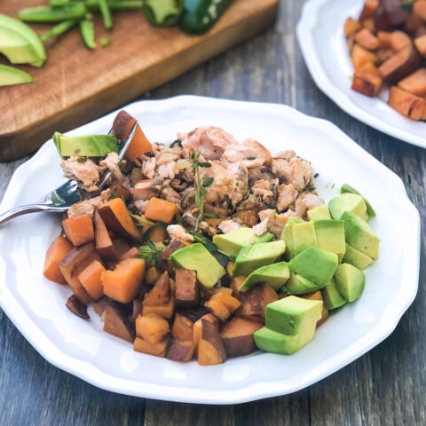 Two bowls of spicy salmon with avocado and sweet potatoes, next to a wooden chopping board with sliced avocado and jalapeño.