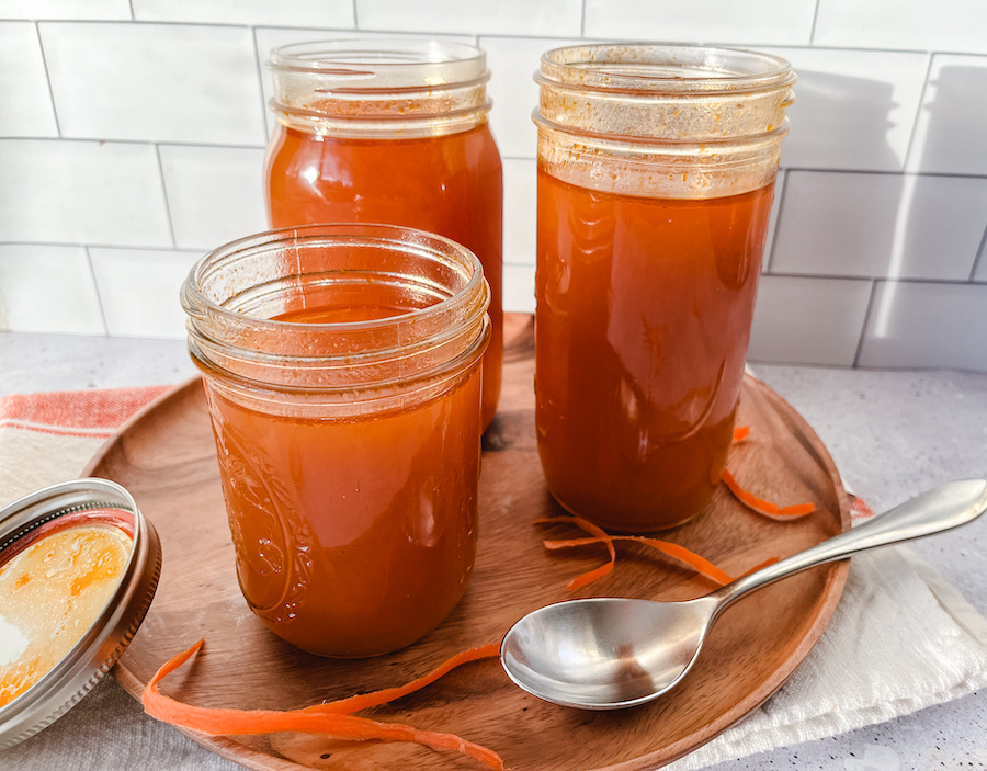 Three mason jars containing vegetable broth on a wooden tray with a silver spoon.