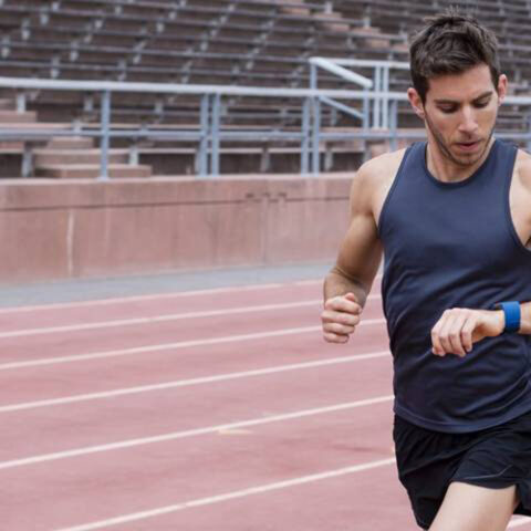 Male runner checking his fitness watch while running on a track.
