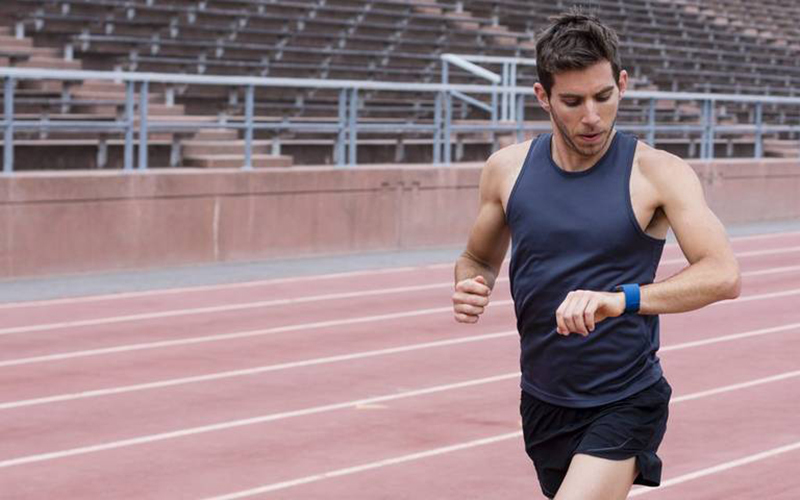 Male runner checking his fitness watch while running on a track.