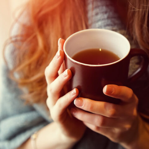 An ill person holds a mug of tea to ease her upset stomach