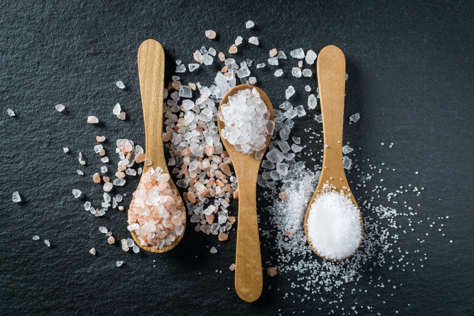 Three spoons with salt crystals on a table: high salt diets can worsen autoimmune conditions