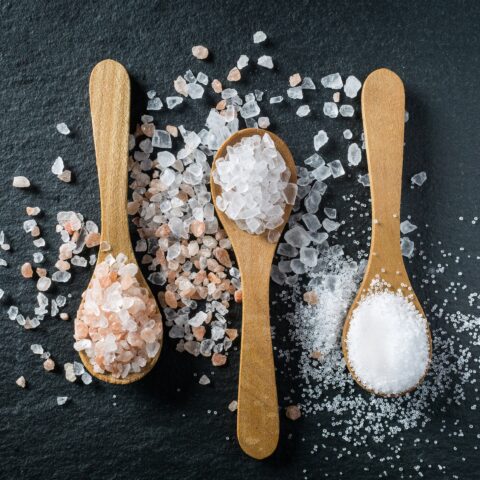 Three spoons with salt crystals on a table: high salt diets can worsen autoimmune conditions