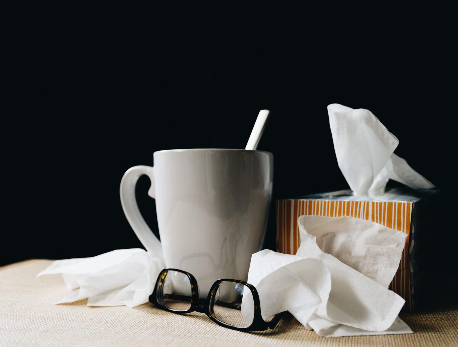 A box of tissues, a hot drink and a pair of reading glasses.