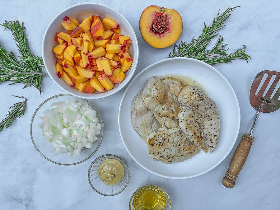 Finished chicken on a plate next to a bowl of chopped peaches, diced onion, and oil.
