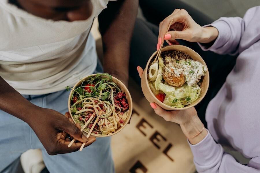 Two people each eating food from a bowl using chopsticks.