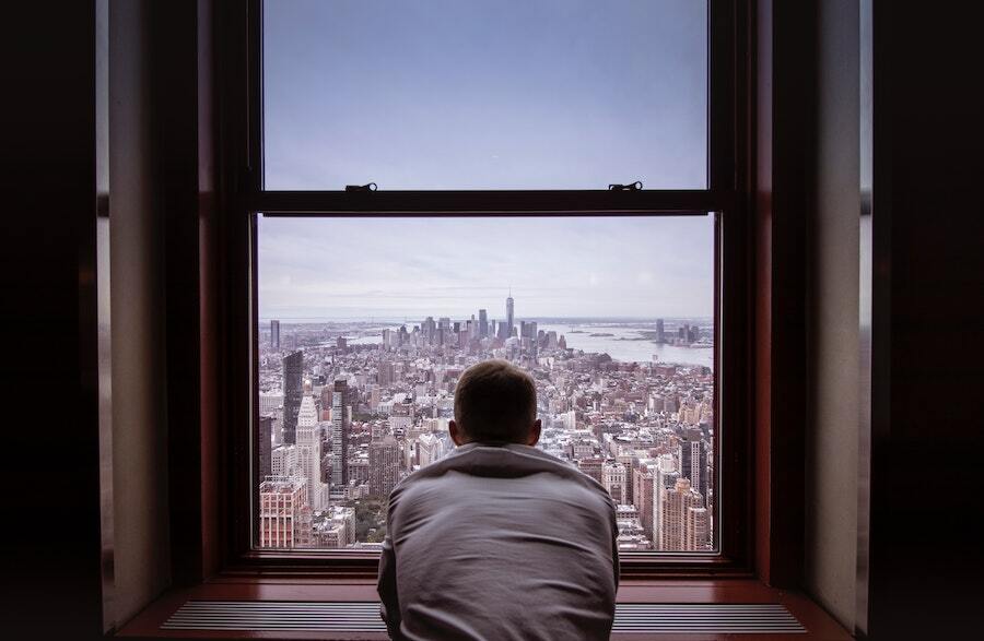 A lone man stairs out of a window at a drab cityscape.
