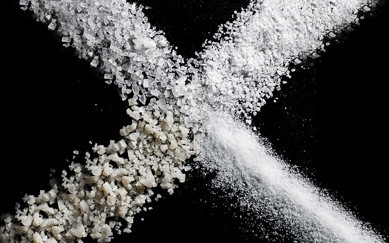 Different types of salt spread on a black background in the shape of an X