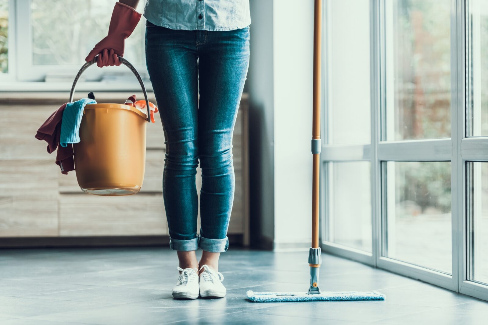 Lower half of a woman with a bucket and sweeper about to clean her home.