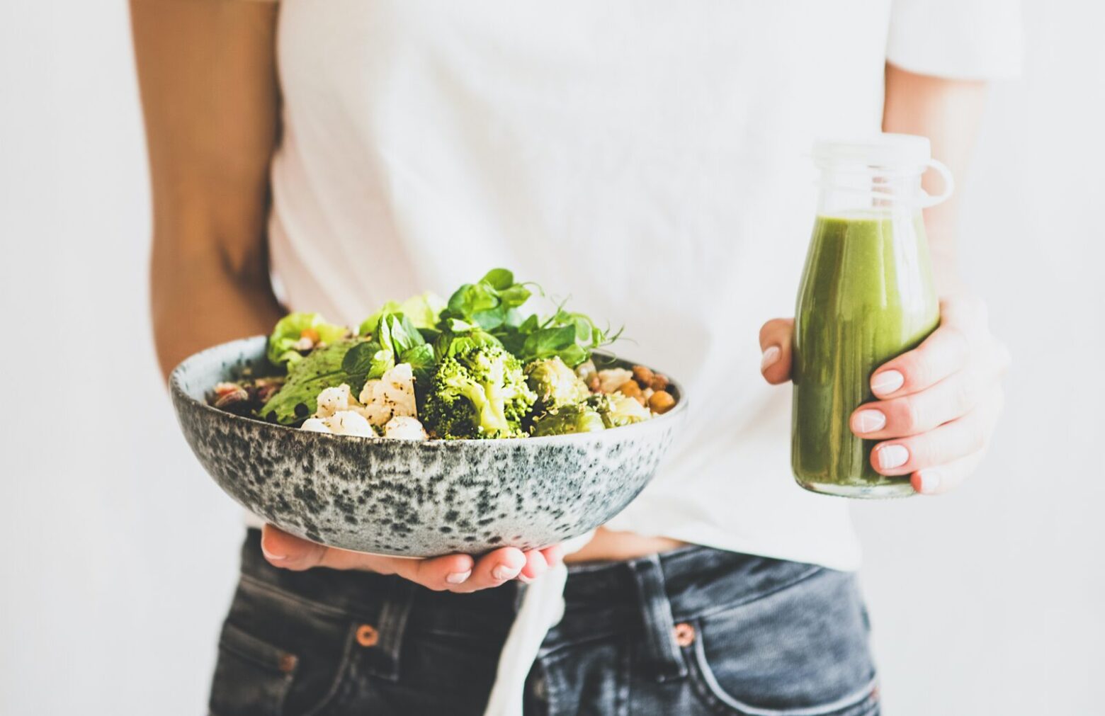 A person holding a bowl of salad and a bottle of green dressing.