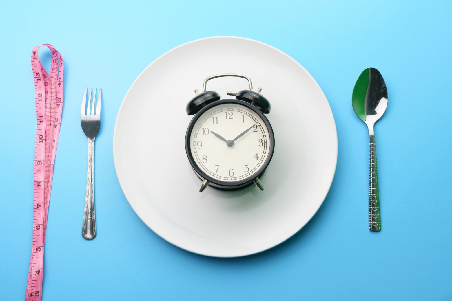 Analog alarm clock on an empty plate with tableware setting