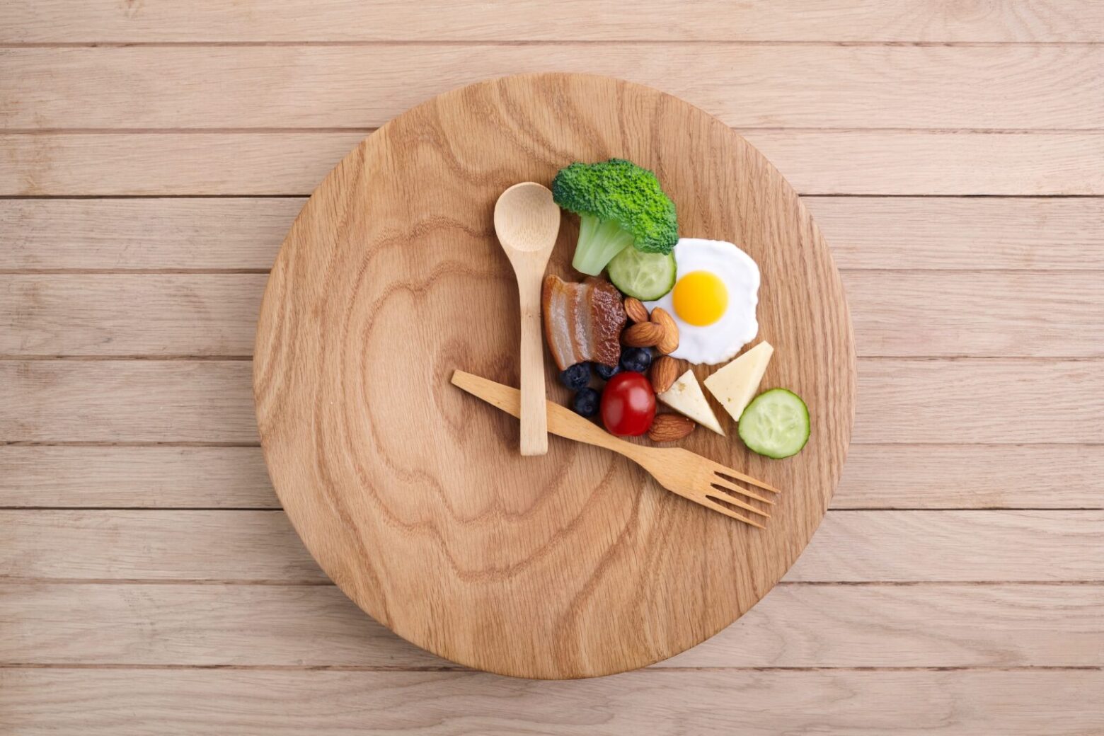 A wooden plate is set with utensils in the shape of a clock with food inside the utensils to indicate an intermittent fasting schedule.