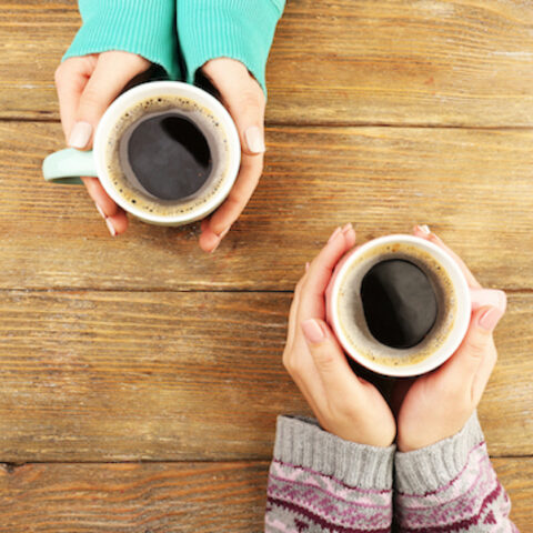Two sets of hands holding coffee in mugs.