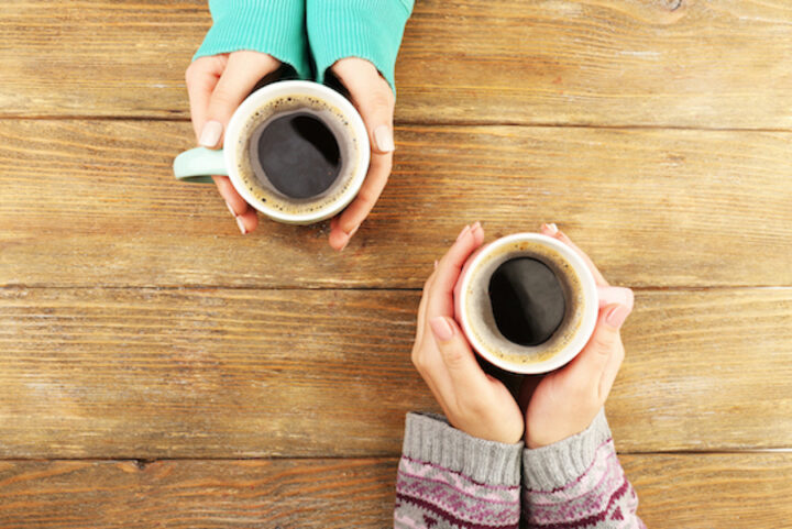 Two sets of hands holding coffee in mugs.