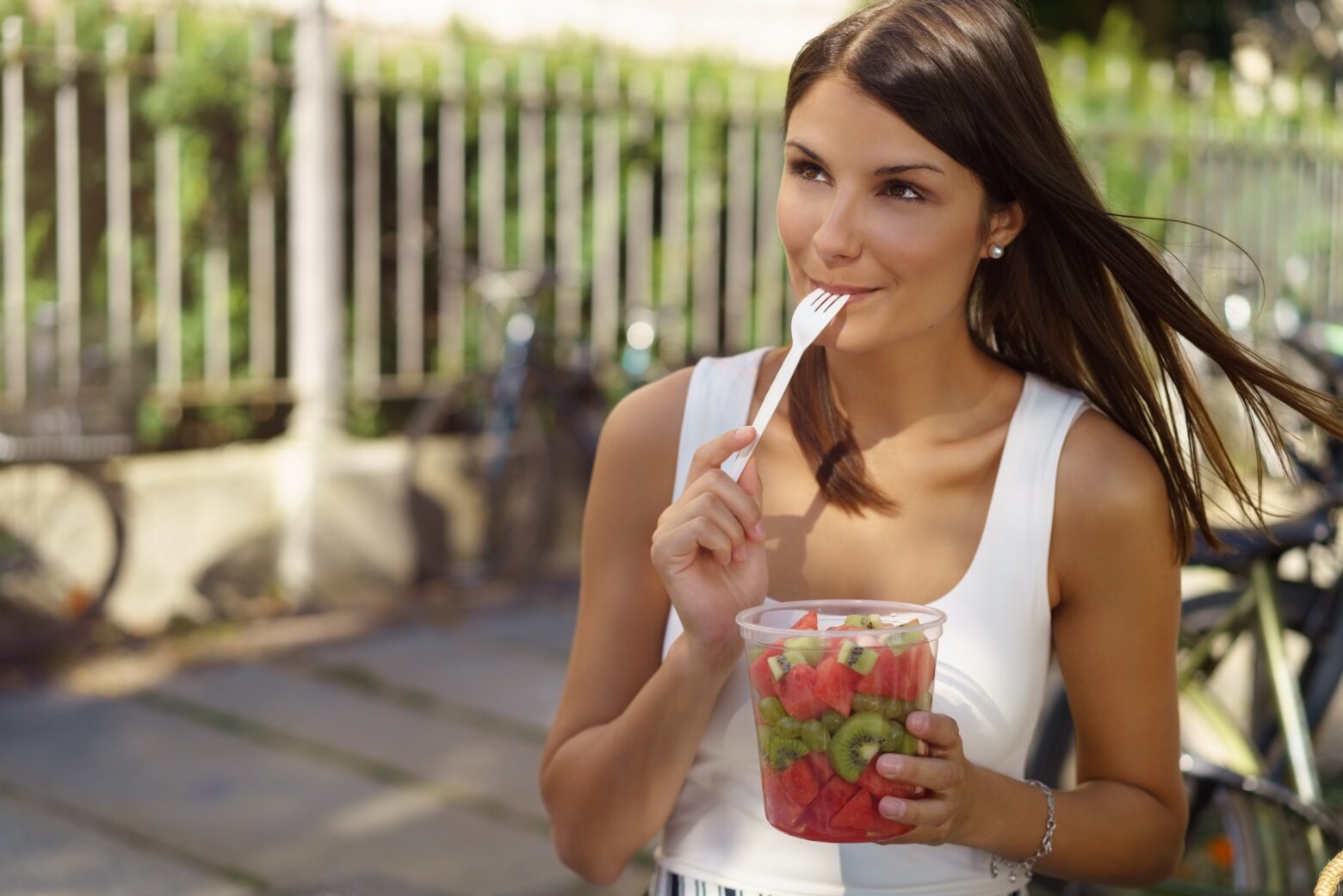 Woman enjoys sliced watermelon and kiwi while sitting outside.