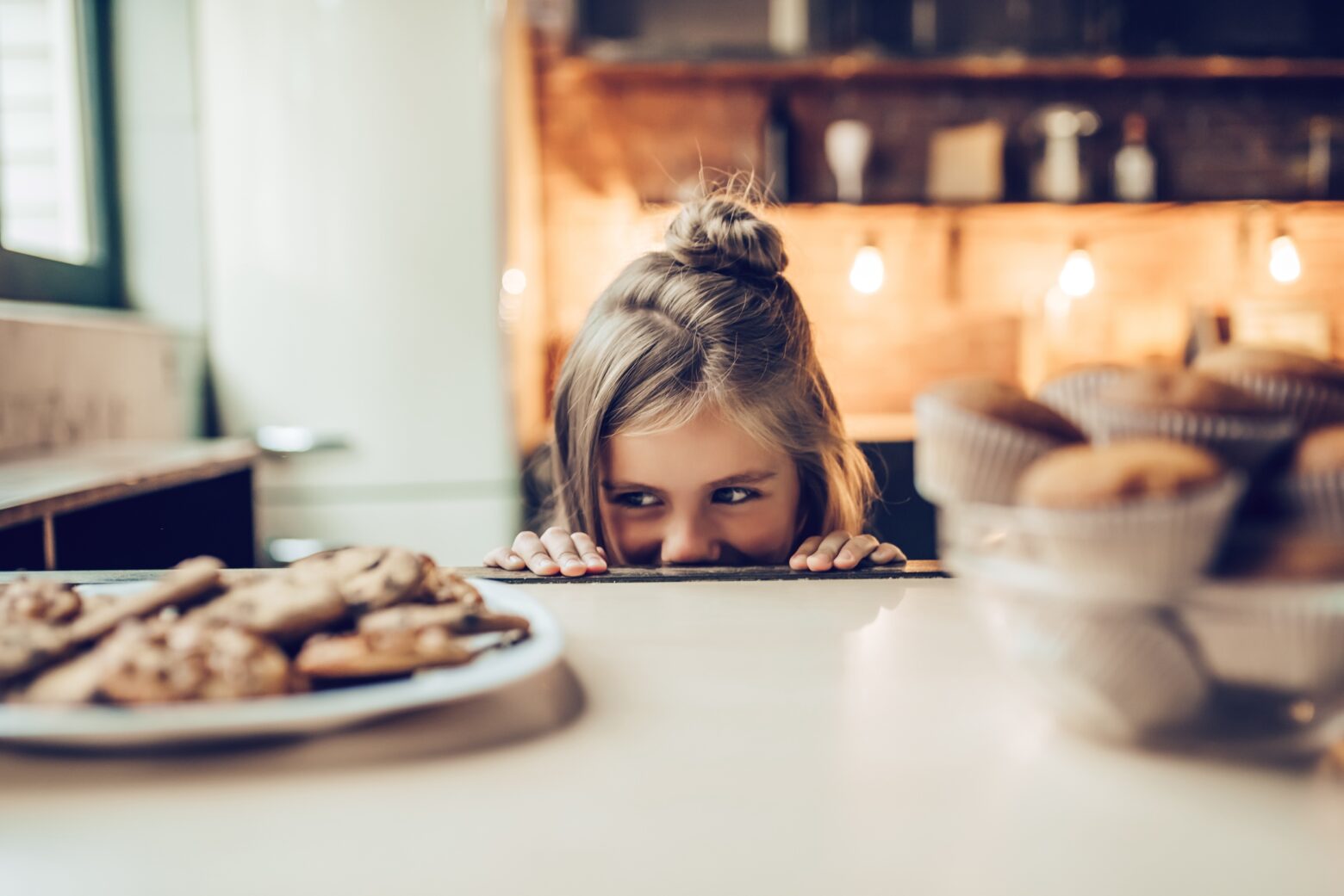 Girl sneakily looking at a plate of cookies on a counter