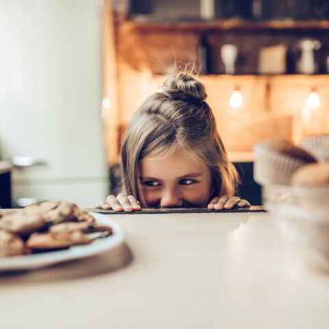 Girl sneakily looking at a plate of cookies on a counter